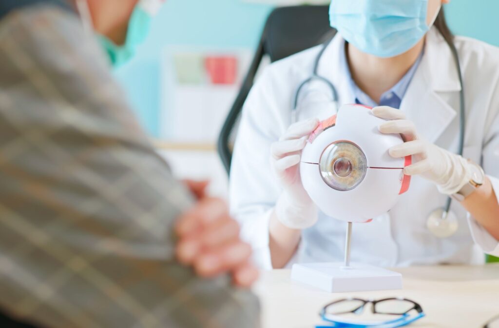 Close up of doctor wearing face mask is showing eyeball model and explaining about eye disease to a patient.