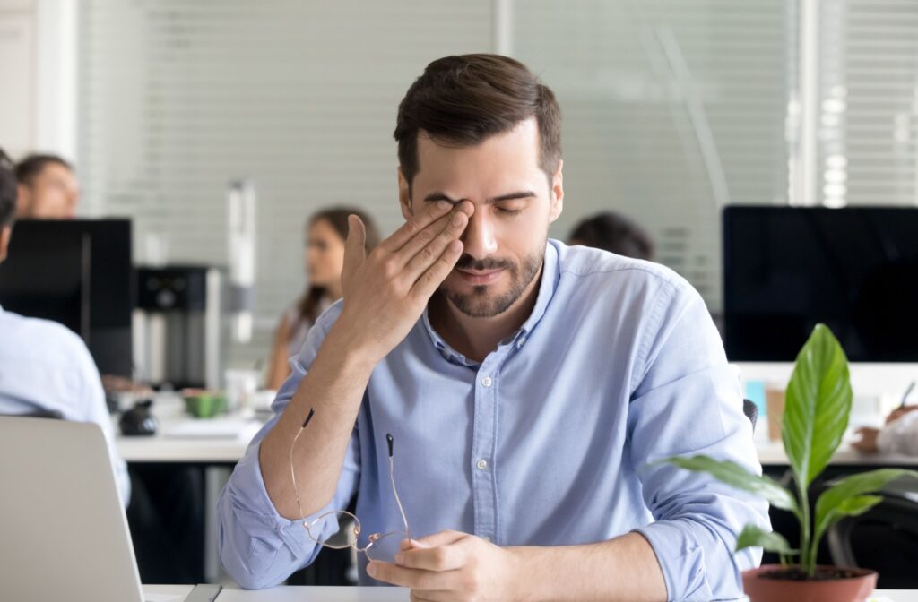 An office worker rubs their dry eye while trying to focus on their computer.