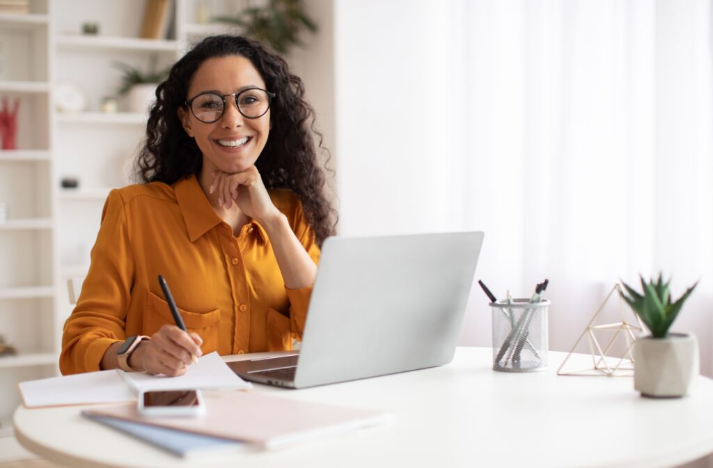 Woman wearing glasses and working on a laptop at a desk.