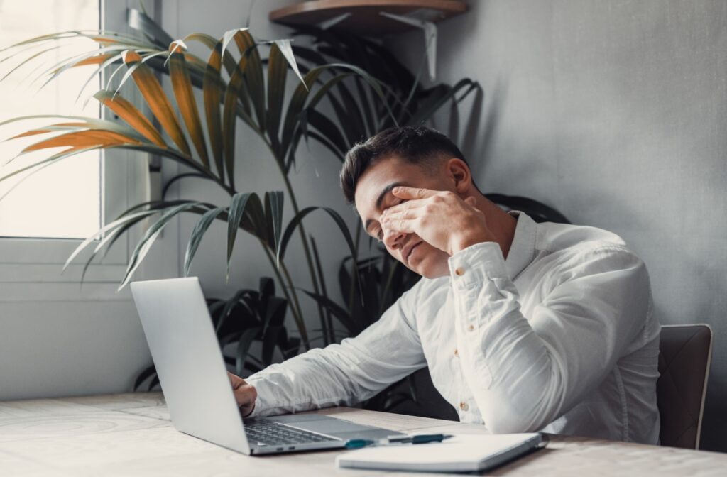 Man rubbing his eyes from digital eye strain while working on a laptop.
