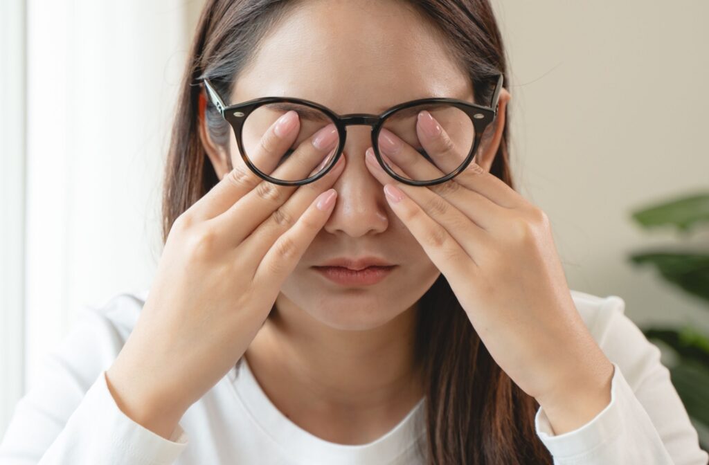 Young woman wearing glasses rubbing her eyes due to dry eye discomfort.