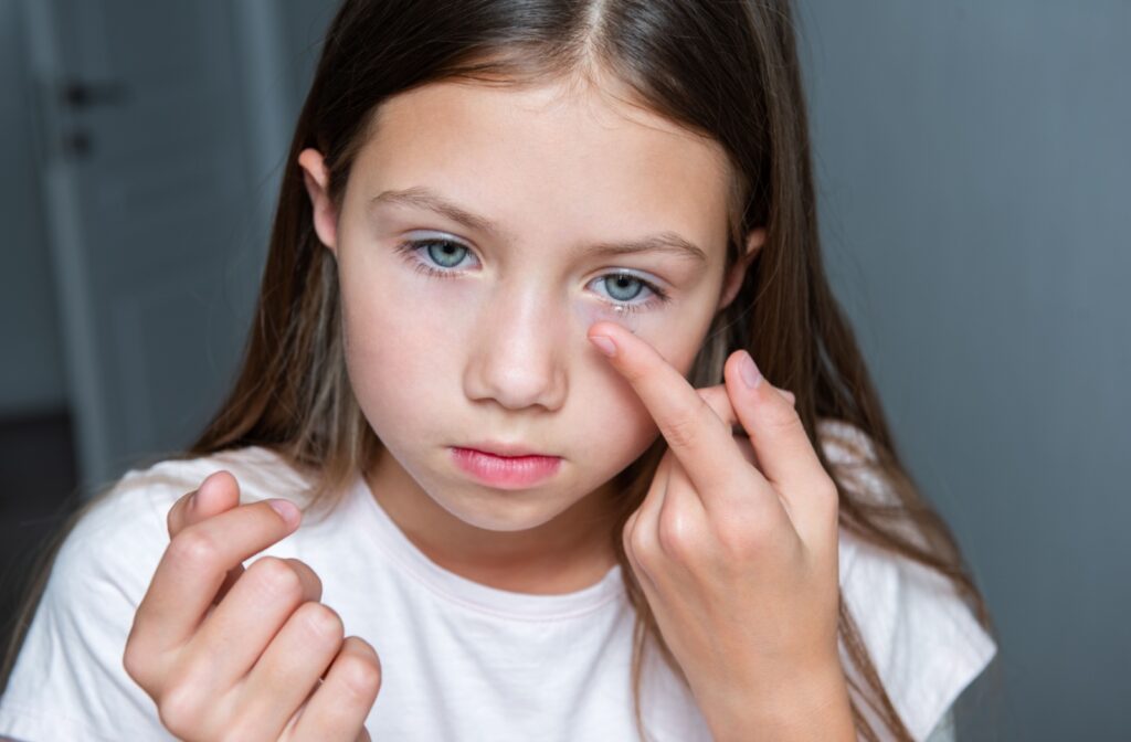 Young girl putting in contact lens into her left eye.